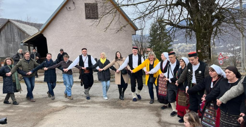 Vairāki cilvēki sadevušies rokās un dejo horvātu apļa deju