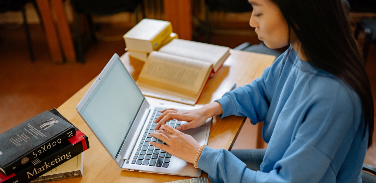 studente mācās bibliotēkā, raksta datorā