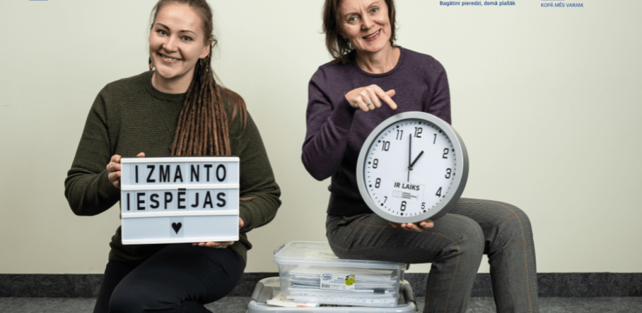 Divas sievietes, viena tur pulksteni, otra tāfeli