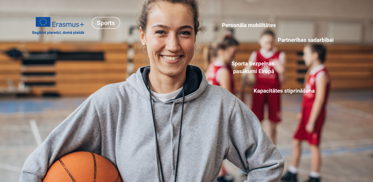 Basketbola trenere ar bumbu rokās, fonā trīs sportisti sarunājas