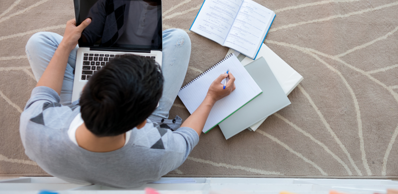 Students sēž uz grīdas ar portatīvo datoru klēpī un veic pierakstus