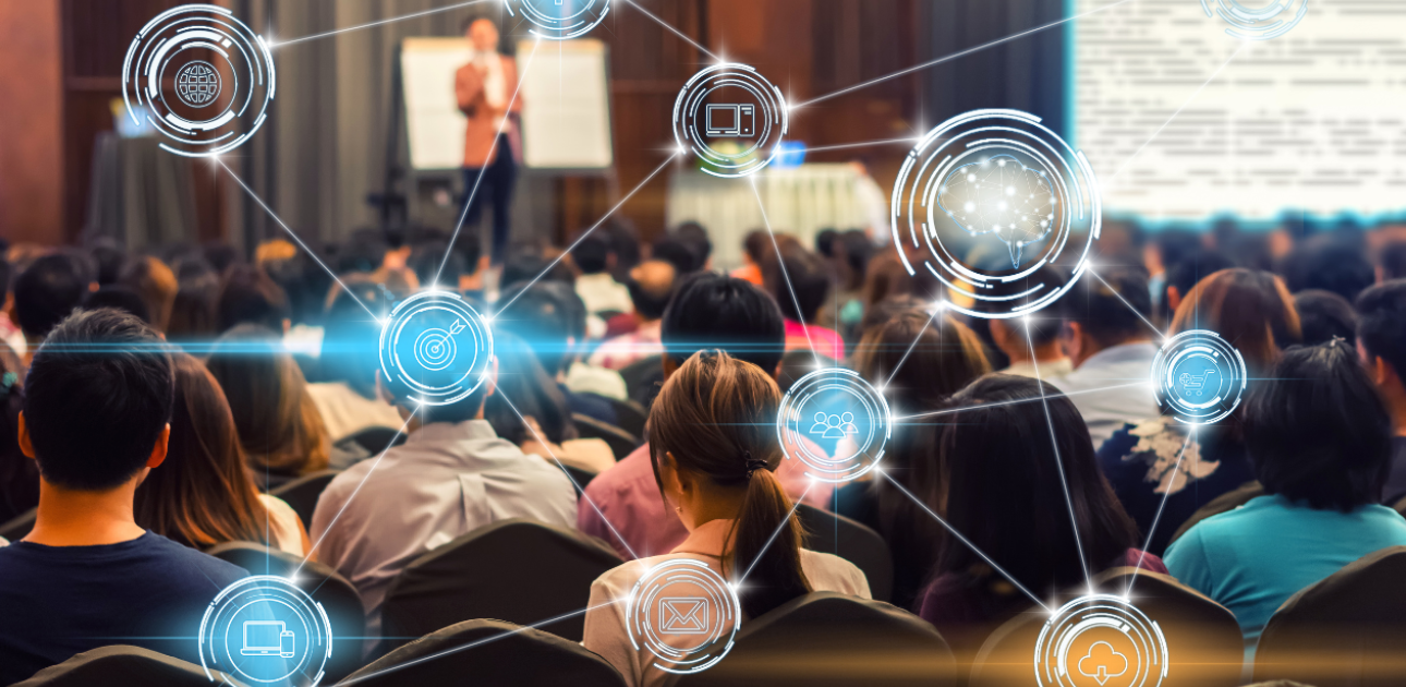 Konferences telpa, kurā sēž daudz cilvēku un uzstājas prezentētājs