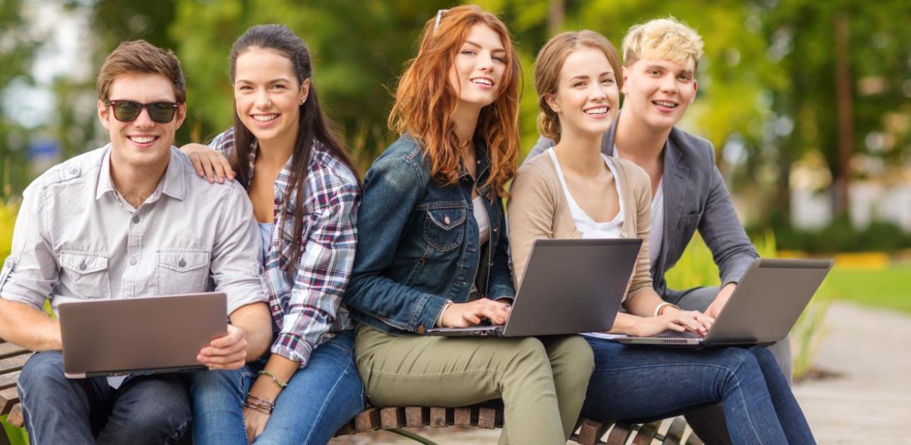Pieci studenti sēž uz soliņa, turot atvērtus klēpjdatorus