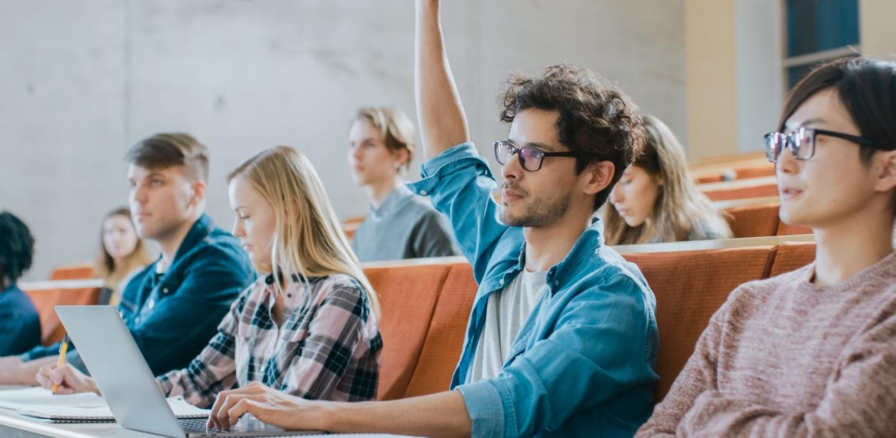 Vairāki studenti sēž auditrijā, viens students pacēlis roku