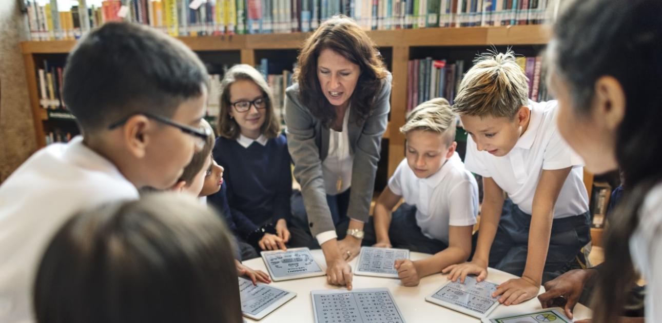 Skolotāja ar skolēniem mācās bibliotēkā matemātiku