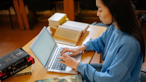 studente mācās bibliotēkā, raksta datorā