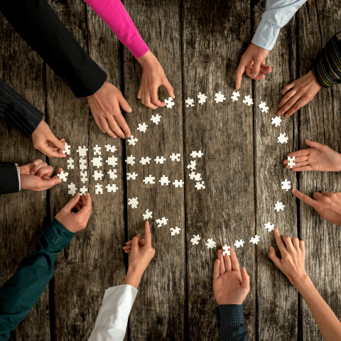 Attēlā redzamas cilvēku plaukstas, kas no puzles gabaliem veido spuldzi